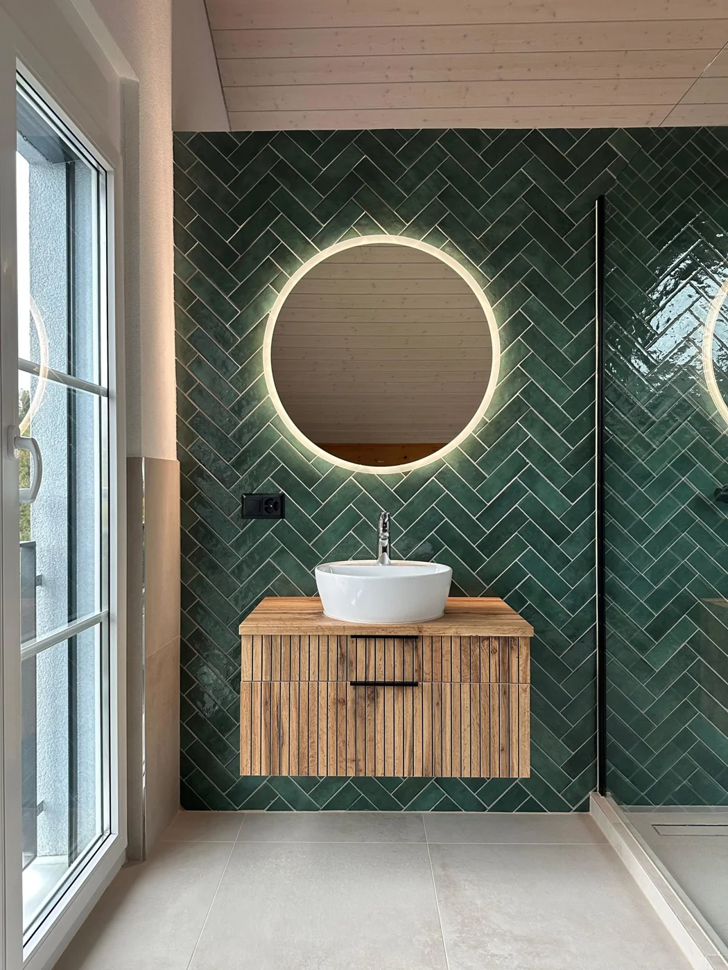 Badezimmer aus dem EA-Portfolio mit grünen Fliesen, rundem Spiegel und Holzwaschtisch
