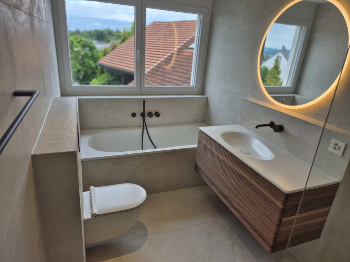 Badezimmer mit Wanne, Waschtisch und rundem Spiegel aus dem EA-Portfolio